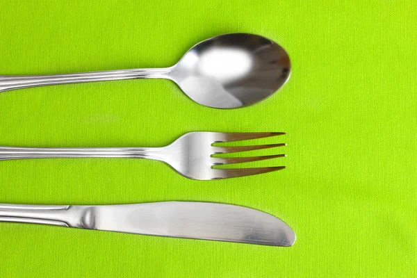 Fourchette, cuillère et couteau sur une nappe verte — Photo