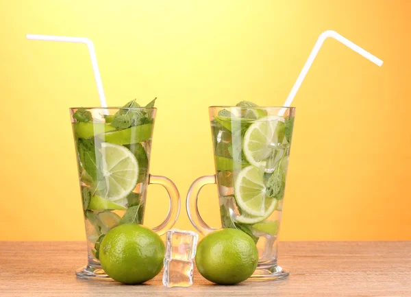 Glasses of cocktail with lime and mint on wooden table on yellow background — Stock Photo, Image