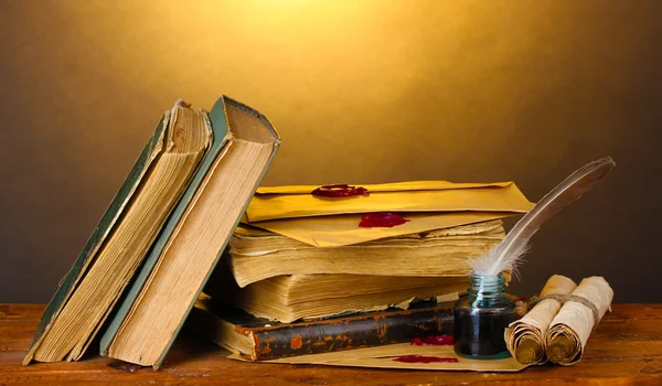 Staré knihy, svitky, peří pero a inkwell na dřevěný stůl na hnědé pozadí — Stock fotografie