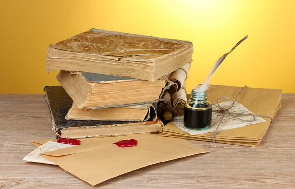 Libri antichi, pergamene, penna piuma e calamaio su tavolo di legno su sfondo giallo — Foto Stock