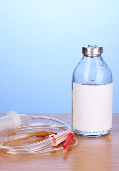 Бутылка внутривенных антибиотиков и пластиковых вливаний на деревянном столе на синем фоне — стоковое фото