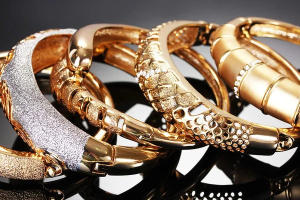 Schöne goldene Armbänder auf grauem Hintergrund — Stockfoto