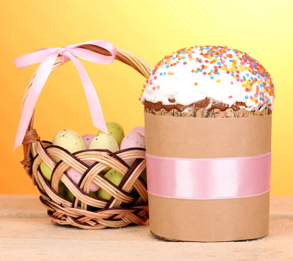 Bolo de Páscoa bonito com ovos na cesta na mesa de madeira no fundo amarelo — Fotografia de Stock