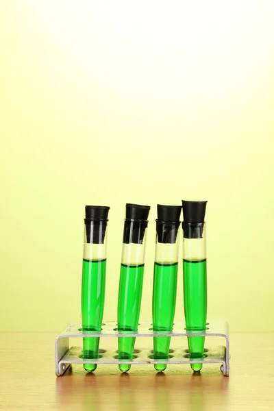 Пробирки с зеленой жидкостью на деревянном столе на зеленом фоне — стоковое фото