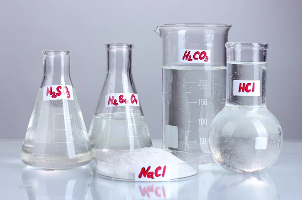 Пробирки с различными кислотами и химикатами на сером фоне — стоковое фото