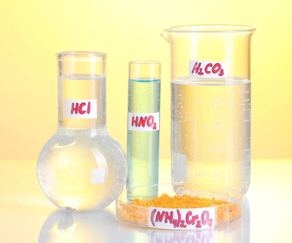 Test-tubes with various acids and chemicals on yellow background — Stock Photo, Image