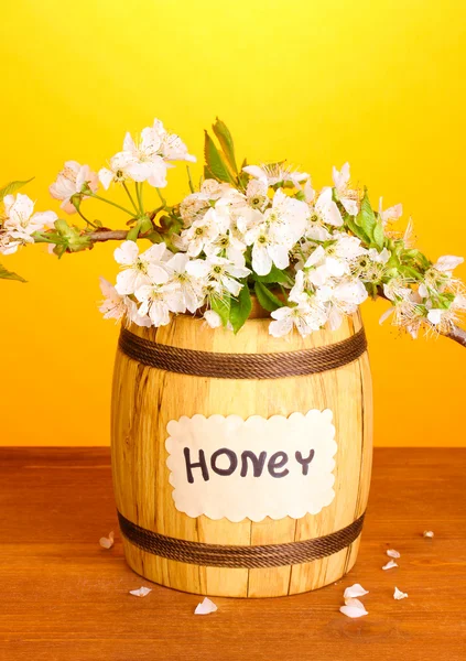 Zoete honing in vat met bloeiende tak op houten tafel op gele achtergrond — Stockfoto