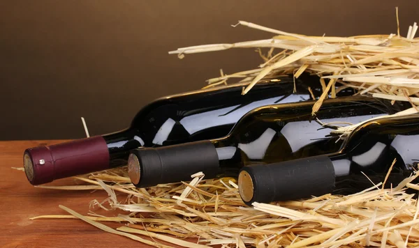 Bottiglie di grande vino su fieno su tavolo di legno su sfondo marrone — Foto Stock