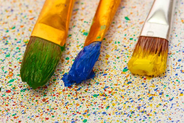 Pincéis com tinta colorida em salpicos coloridos fundo close-up — Fotografia de Stock