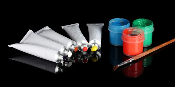 Tubes with colorful watercolors and jars with gouache and brush on black background close-up — Stockfoto