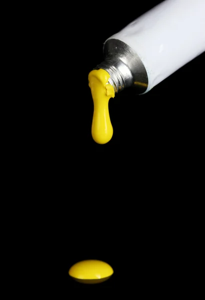 Gelbe Farbe folgt aus der Tube auf schwarzem Hintergrund in Nahaufnahme — Stockfoto