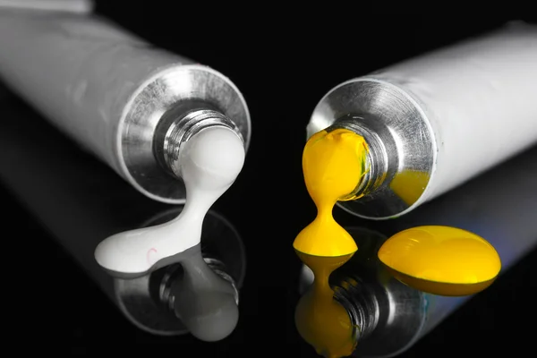 White and yellow paints follow from the tubes on black background close-up — Stock Photo, Image