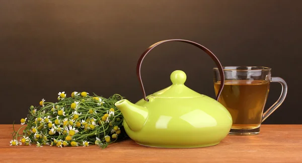 Teekanne und Tasse mit Kamillentee auf Holztisch auf braunem Hintergrund — Stockfoto