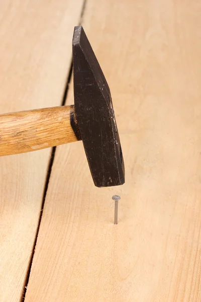 Metal nail in wooden plank and hammer — Stock Photo, Image