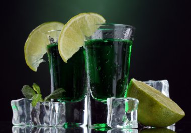 Two glasses of absinthe, lime and ice on green background clipart