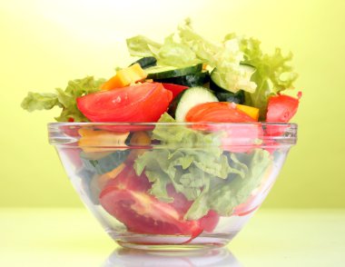 Fresh vegetable salad in transparent bowl on green background clipart