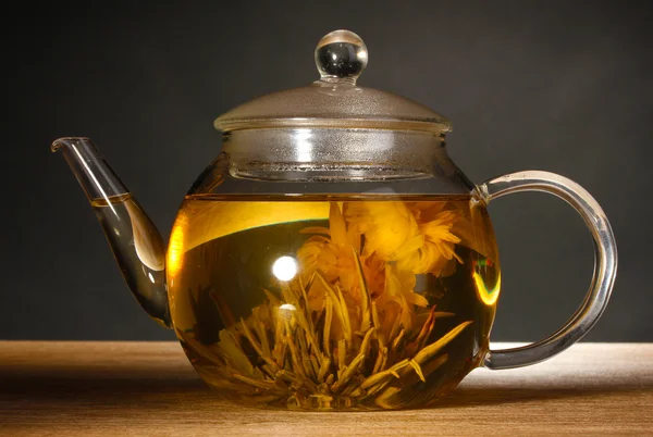 Glas-Teekanne mit exotischem grünen Tee auf Holztisch auf grauem Hintergrund — Stockfoto