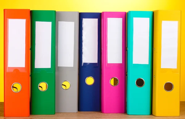 Яркие офисные папки на деревянном столе на желтом фоне — стоковое фото