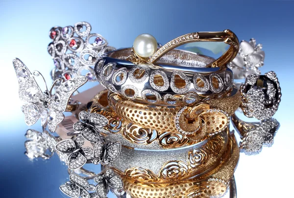 Schöne silberne und goldene Armbänder und Ringe auf blauem Hintergrund — Stockfoto