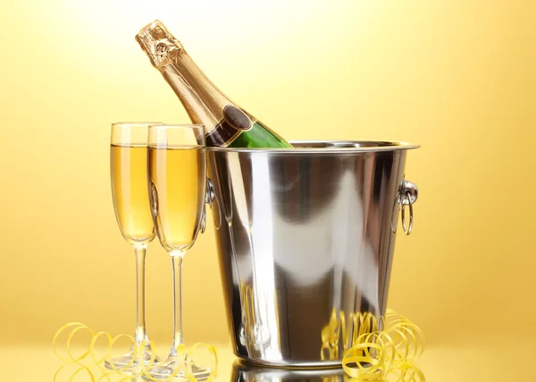 Bouteille de champagne dans un seau avec glace et verres de champagne, sur fond jaune — Photo