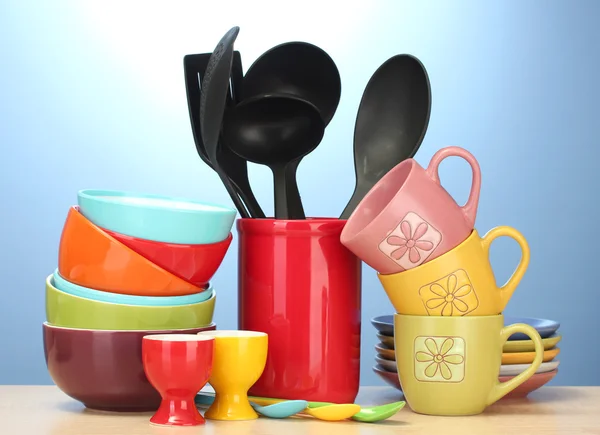 Ciotole vuote luminose, tazze e utensili da cucina su tavolo in legno su sfondo blu — Foto Stock