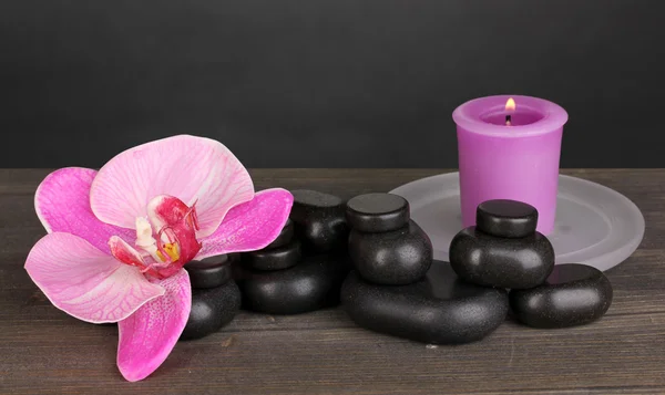 水疗中心的石头与兰花花和灰色的背景上的木桌上的蜡烛 — 图库照片