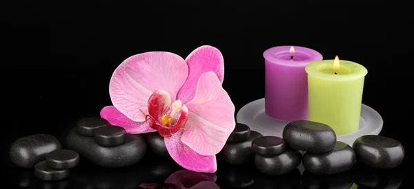 Курортные камни с цветком орхидеи и свечами, изолированными на черном — стоковое фото