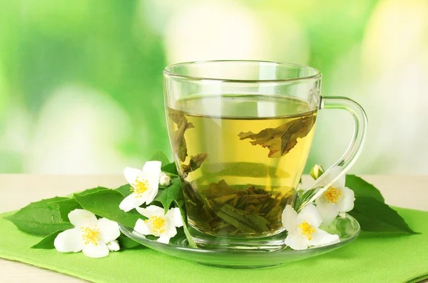Xícara de chá verde com flores de jasmim na mesa de madeira no fundo verde — Fotografia de Stock