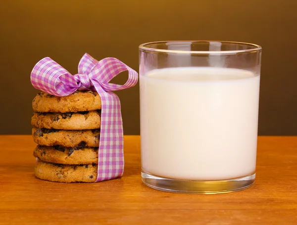 Sklenici mléka a soubory cookie na dřevěný stůl na hnědé pozadí — Stock fotografie