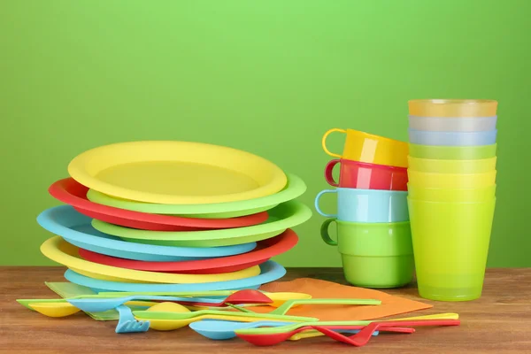Jasne plastikowe naczynia jednorazowe na drewnianym stole na kolorowe tło — Zdjęcie stockowe