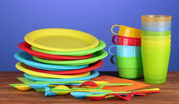 Яркая пластиковая одноразовая посуда на деревянном столе на красочном фоне — стоковое фото