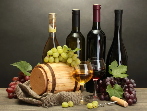 Barril, botellas y copas de vino y uvas maduras sobre mesa de madera sobre fondo gris —  Fotos de Stock