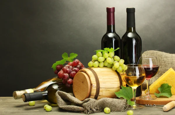 Fat, flaskor och glas vin, ost och mogna druvor på träbord på grå bakgrund — Stockfoto
