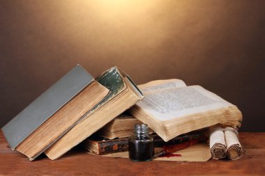 Old books, scrolls, ink pen and inkwell on wooden table on brown background clipart