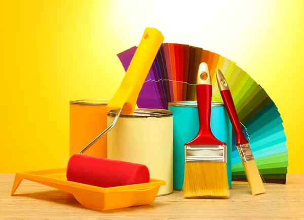 Latas con pintura, rodillo, pinceles y paleta de colores sobre tabla de madera sobre fondo amarillo — Foto de Stock