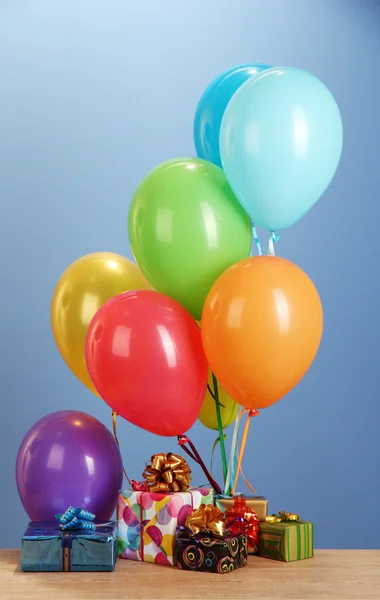 Kleurrijke ballonnen houden een geschenken op een houten tafel op blauwe achtergrond — Stockfoto