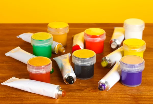 Tubi con acquerelli colorati e vasetti con guazzo su tavolo in legno su sfondo giallo brillante — Foto Stock