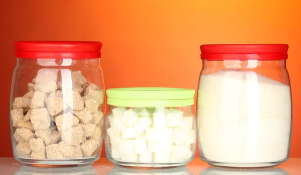 Frascos con terrón de azúcar de caña morena, azúcar de cristal blanco y azúcar de terrón blanco sobre fondo colorido — Foto de Stock