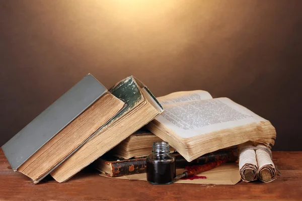 Oude boeken, rollen, inkt pen en inktpotje op houten tafel op bruine achtergrond — Stockfoto