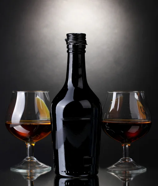 Glazen van brandy en fles op grijze achtergrond — Stockfoto