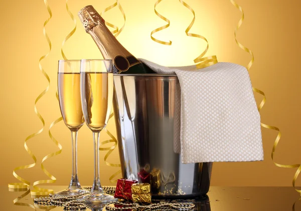 Bottiglia di champagne in secchio con ghiaccio e bicchieri di champagne, su fondo giallo — Foto Stock