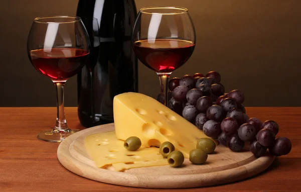 Flasche großer Wein mit Weingläsern und Käse auf Holztisch auf braunem Hintergrund — Stockfoto