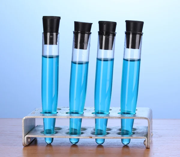 Tubes à essai avec liquide bleu sur table en bois sur fond bleu — Photo