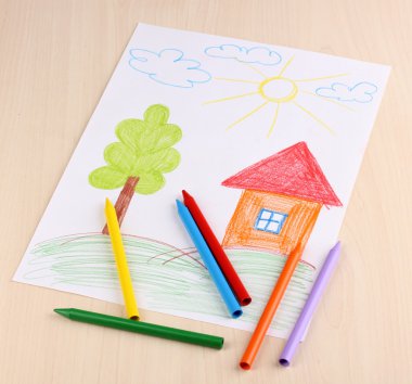 Children's drawing of house and pencils on wooden background clipart