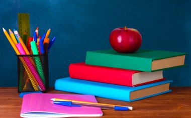 Composition of books, stationery and an apple on the teacher's desk in the background of the blackboard clipart