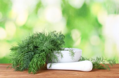 Dill in a mortar and pestle on green background clipart