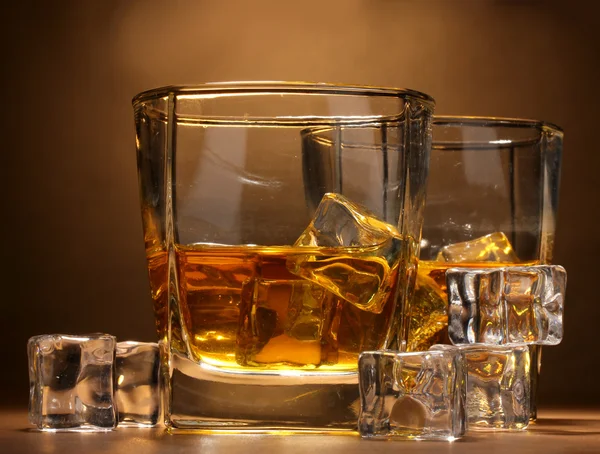 Two glasses of scotch whiskey and ice on wooden table on brown background — Stock Photo, Image