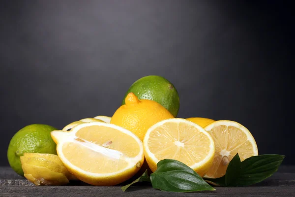Zralé citrony a limetky s listy na dřevěný stůl na šedém pozadí — Stock fotografie