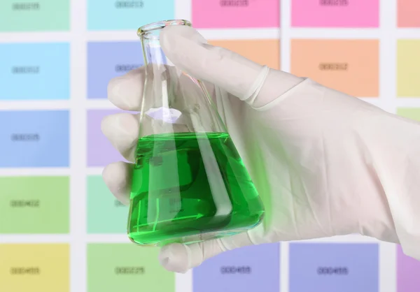 Flask with green liquid in hand on color samples background — Stock Photo, Image