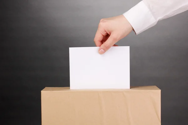 投票の投票用紙と灰色の背景上のボックスを持つ手します。 — ストック写真